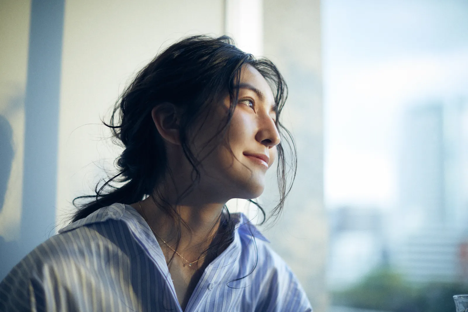 窓辺の光の中で外を見る、ウェーブヘアの女性|THE BALCONY のスタイル